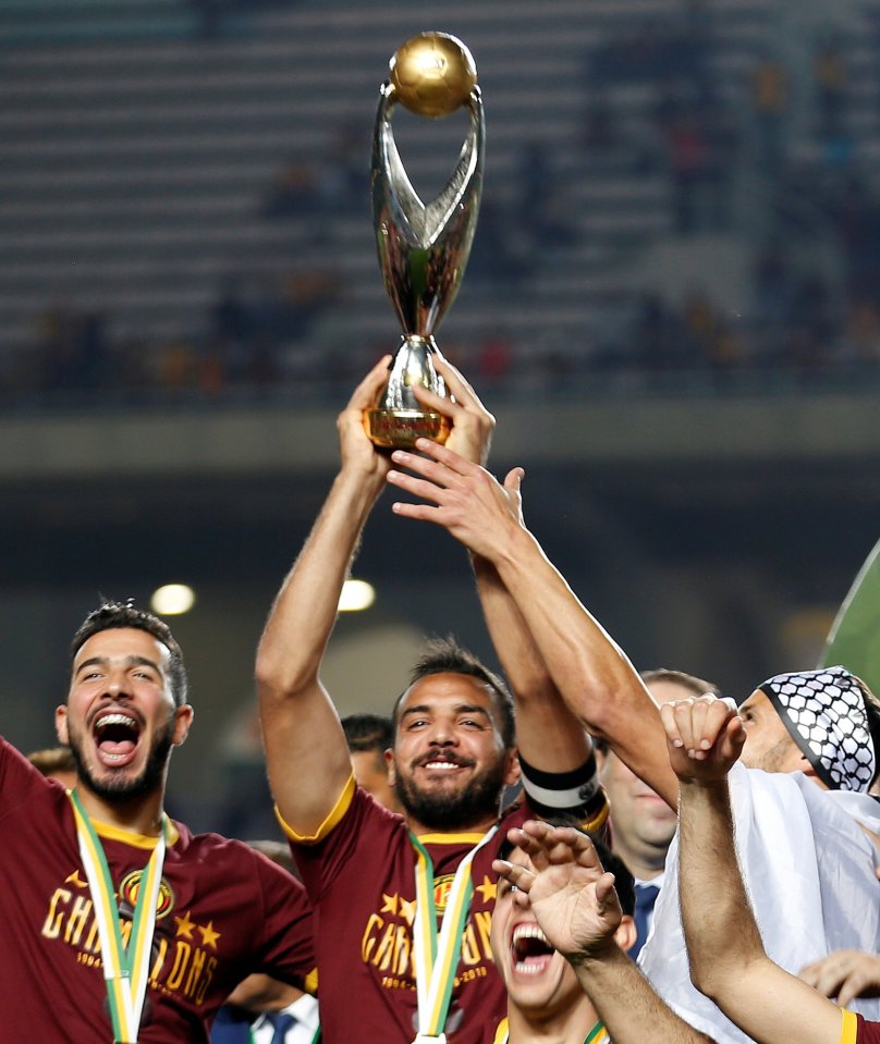 A soccer player raising the African Champions League trophy above his head.